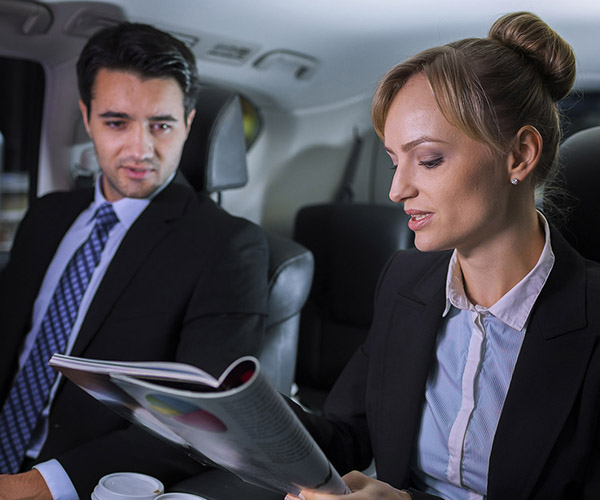 Two young business exectuives talking about a progress report while traveling in a luxury vehicle