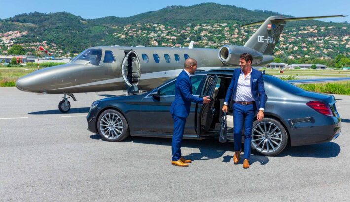 Two professionals standing infornt of a limo and an aeroplane